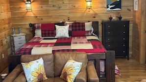 Una habitación acogedora con una cama, dos luces fijadas a la pared, un aparador y una pared de madera.