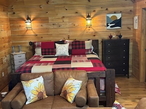 A cozy room with a bed, two wall-mounted lights, a dresser, and a wooden wall.