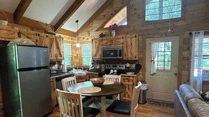 Una cocina de estilo rústico tipo cabaña, con gabinetes de madera, un refrigerador, una estufa y un comedor con sillas y una mesa.
