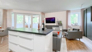 Cozinha moderna com uma ilha grande, área de jantar com sofá cinzento e televisão de tela plana na parede.