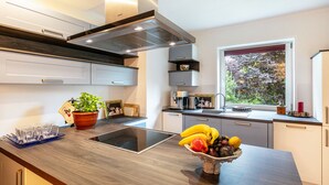 Uma cozinha moderna com fogão embutido, janela com vista para árvores e uma fruteira no balcão.