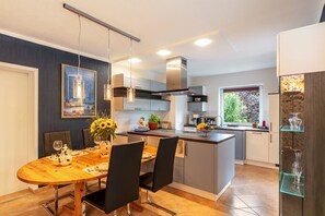Una cocina moderna con una isla central, paredes azul oscuro y un comedor con mesa y sillas de madera.