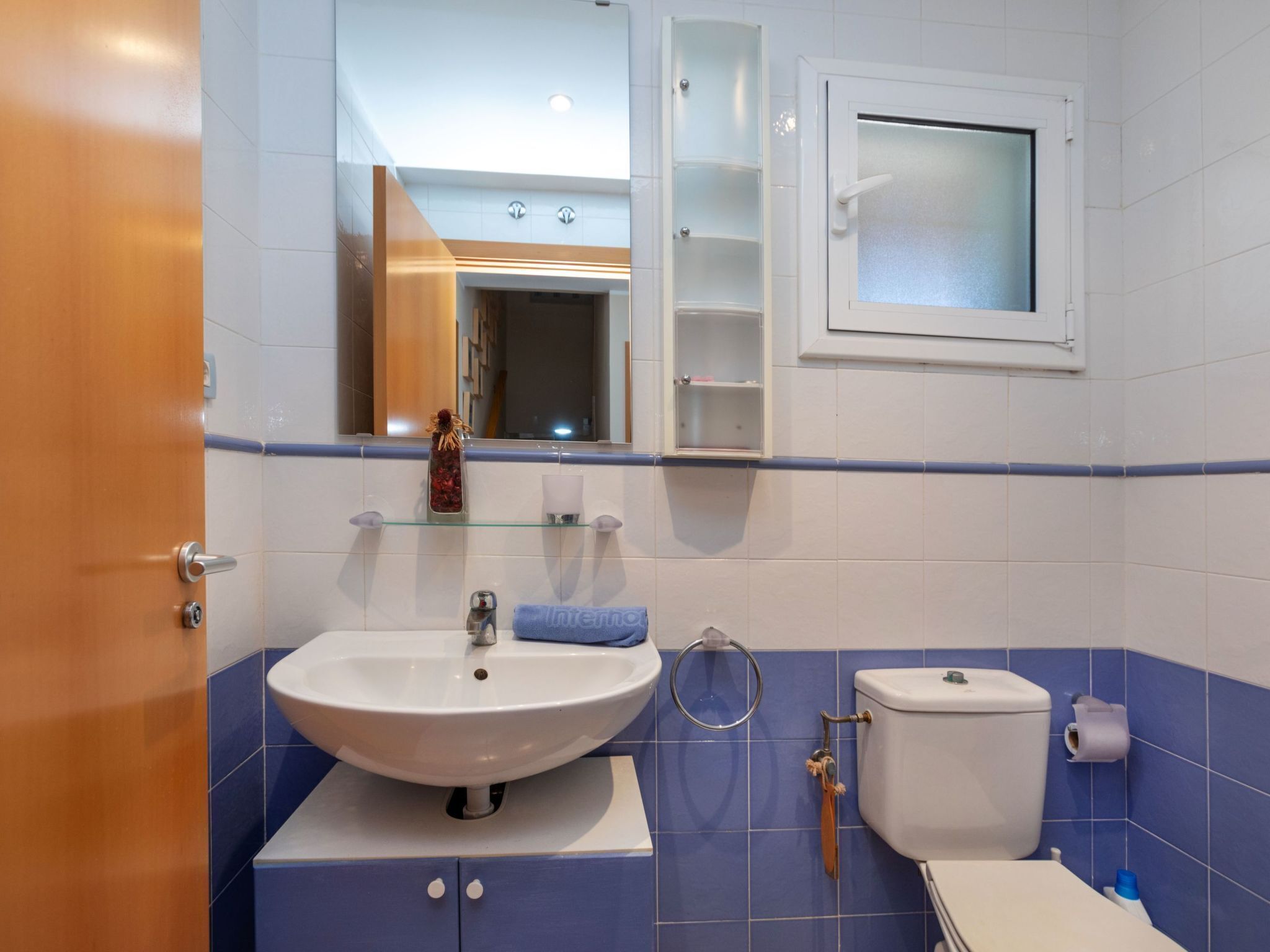 A bathroom with a white sink, blue-tiled walls, a toilet, and a mirror above the sink.