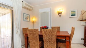 Un coin repas avec une table en bois et des chaises en osier, une lampe fixée au mur et un tableau encadré.