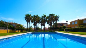 Une piscine à l’eau d’un bleu cristallin, entourée de palmiers et avec un bâtiment jaune en arrière-plan.