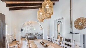 Un vaste salon doté d’une grande table à manger en bois, de chaises blanches et d’un lustre moderne.