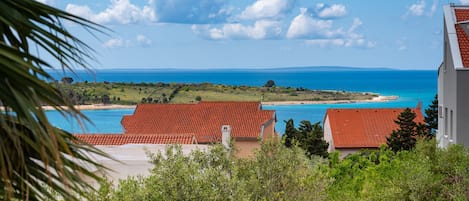 A coastal view with red-roofed buildings, a clear sky, and a distant shoreline.