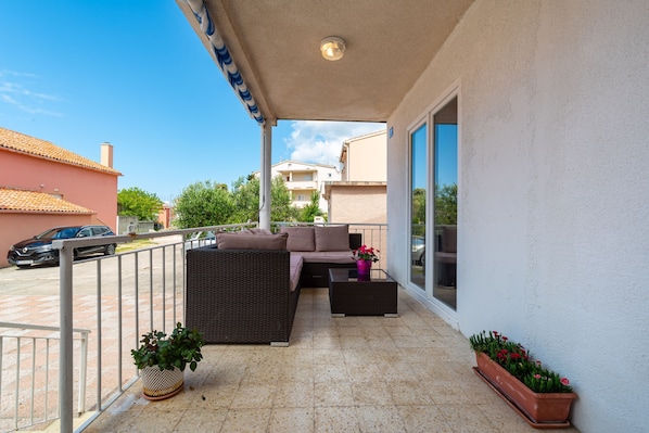 A balcony with a wicker sofa, a small table, and potted plants.