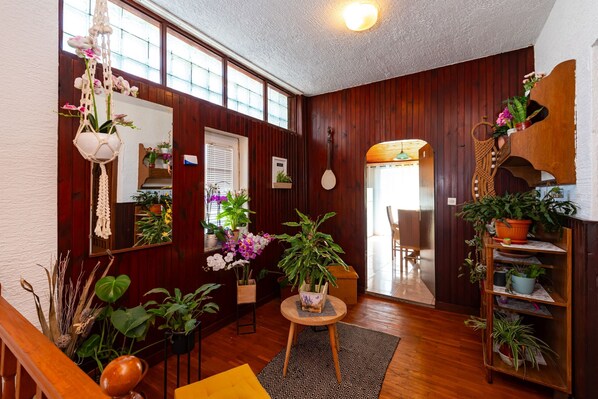 A room with wooden walls, a wooden staircase, a round table with a plant, and a bookshelf with plants.