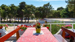 A terrace with a red patterned tablecloth, wooden benches, and potted plants with red flowers.