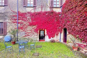 Un patio con una mesa y sillas, una planta en maceta e un edificio cubierto de hiedra roja.