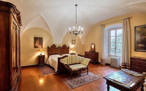 Un dormitorio con una cama grande, un sofá, un aparador de madera, una mesa y una araña.
