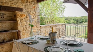 A table set for dining with a bottle of wine, glasses, and plates, set against a stone wall with a view of greenery. - Beautiful holiday home with a shared pool (Dégagnac)