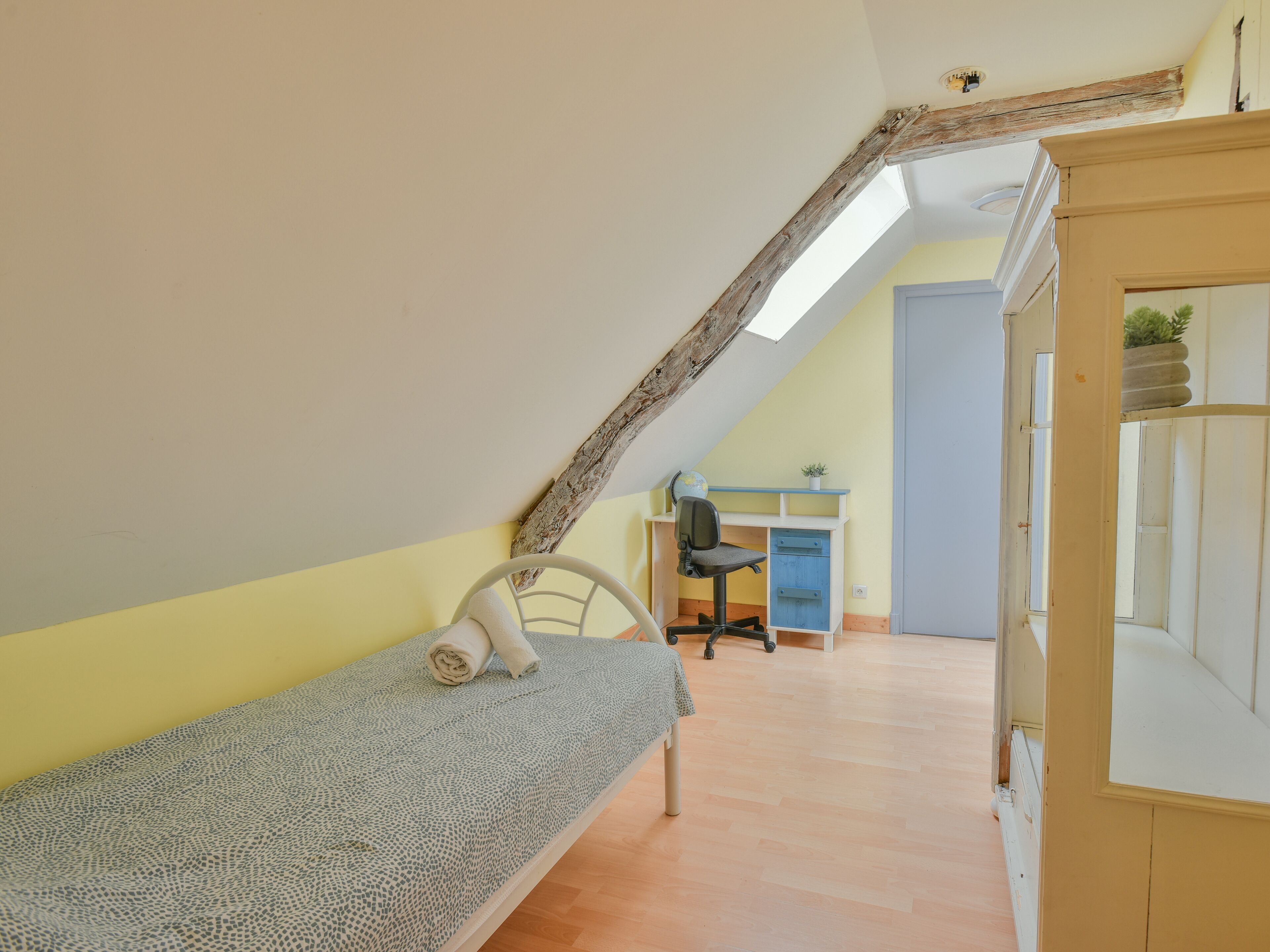 Une petite pièce agréable, avec un plafond en pente, un lit simple, un bureau avec une chaise et une fenêtre.