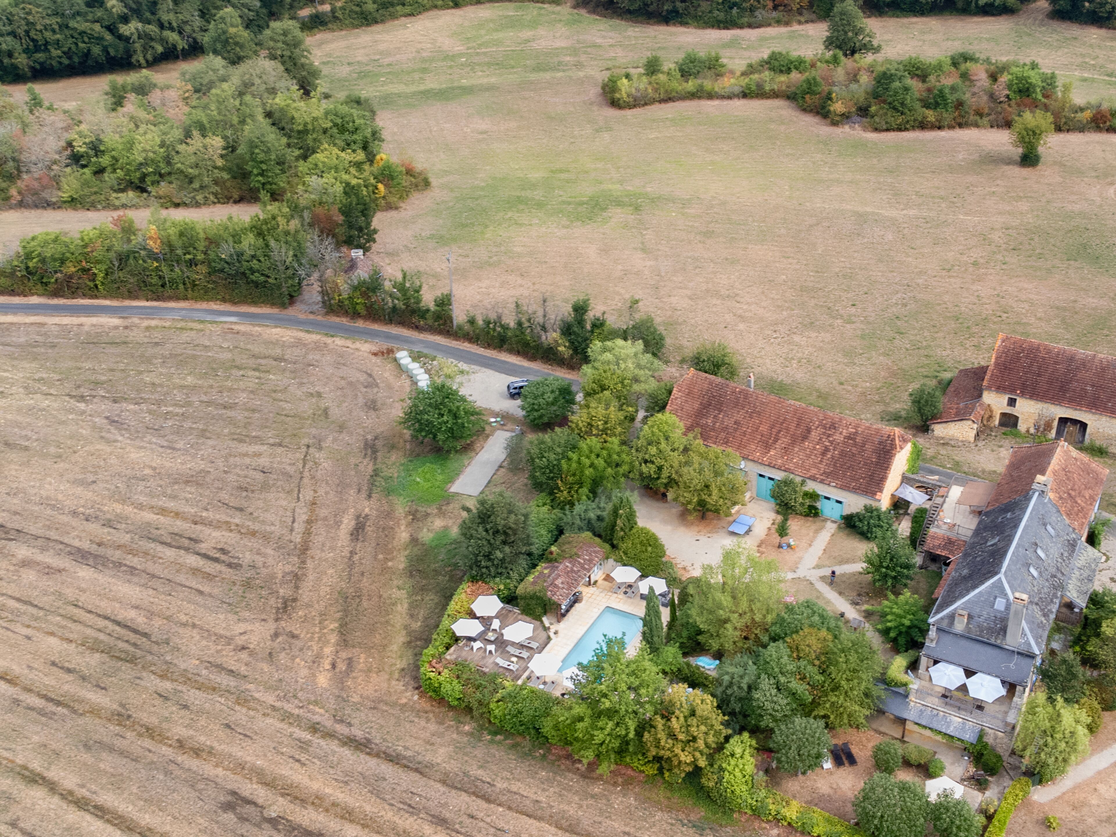 An aerial view of a rural property with multiple buildings, a swimming pool, and surrounding fields.