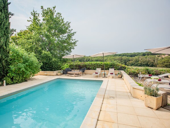 A swimming pool with lounge chairs and umbrellas, surrounded by greenery and a view of hills. - Beautiful holiday home with a shared pool (Dégagnac)