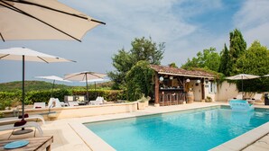 Zona de piscina con sillones de descanso, sombrillas y bar.