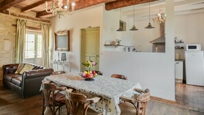 Un comedor rústico con una mesa de madera, sillas y una araña. Se ve una cocina al fondo.