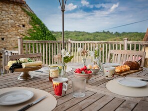 A wooden table set for breakfast with various food items and drinks, overlooking a scenic landscape. - Cosy family home with a shared pool (Dégagnac)