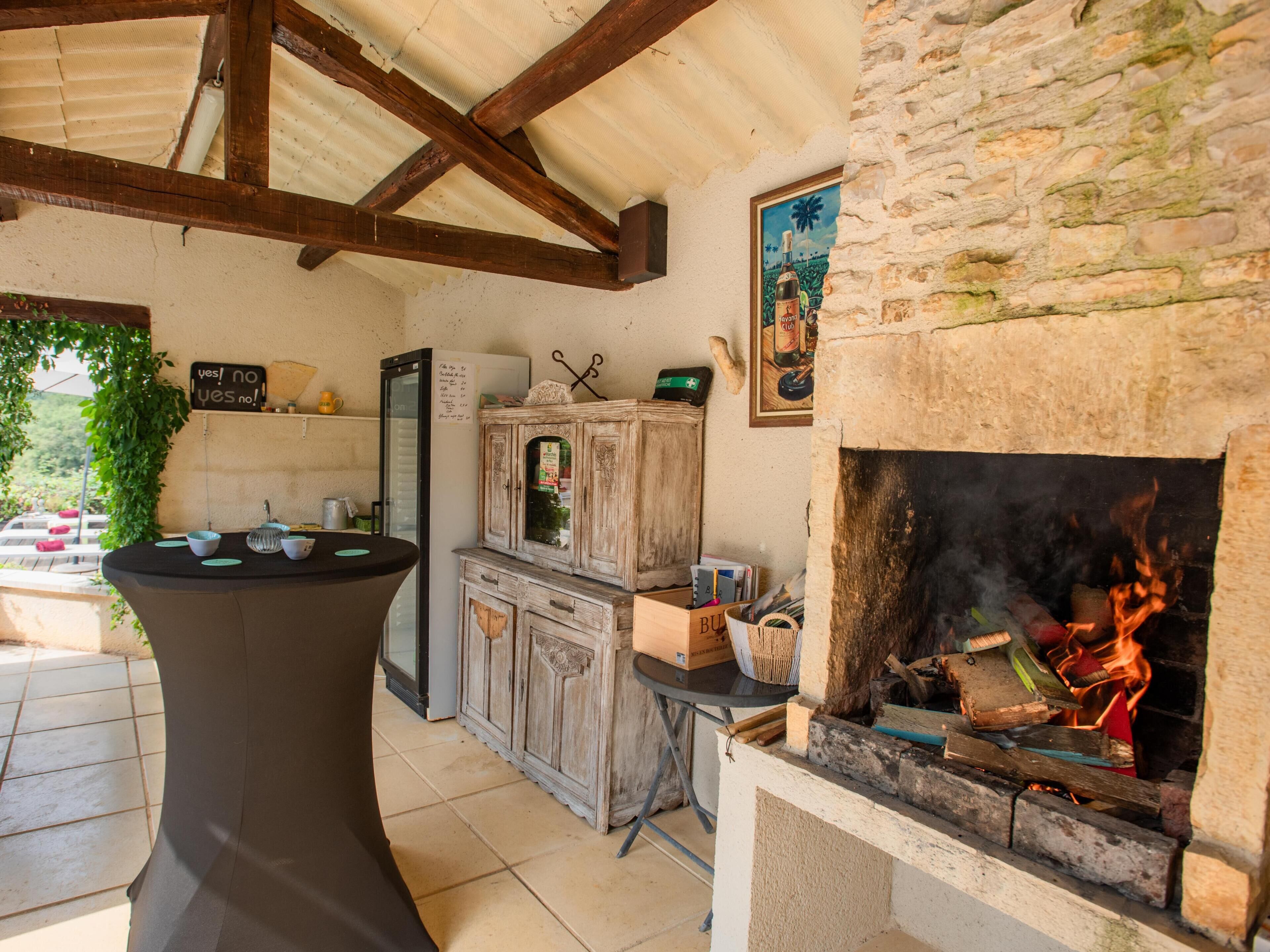 A rustic outdoor kitchen with a stone fireplace, wooden cabinets, and a black table with bowls.