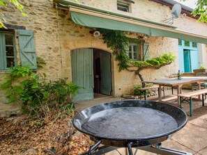 A stone building with a covered patio, a large outdoor grill, and a dining table.