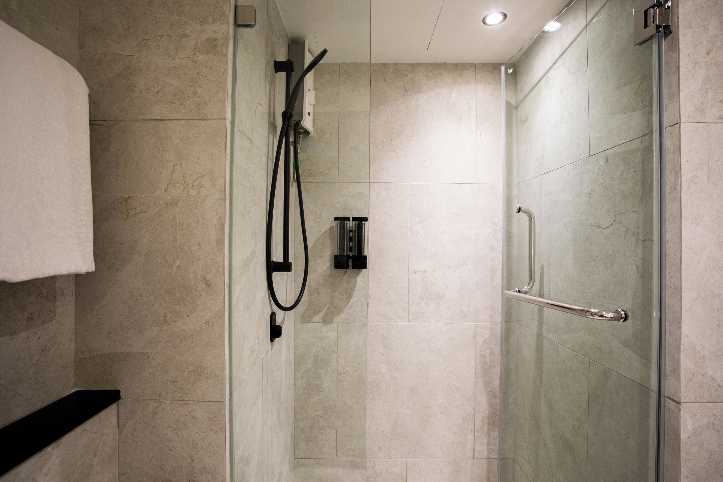 A glass-enclosed shower with a handheld showerhead and a handheld shower attachment.