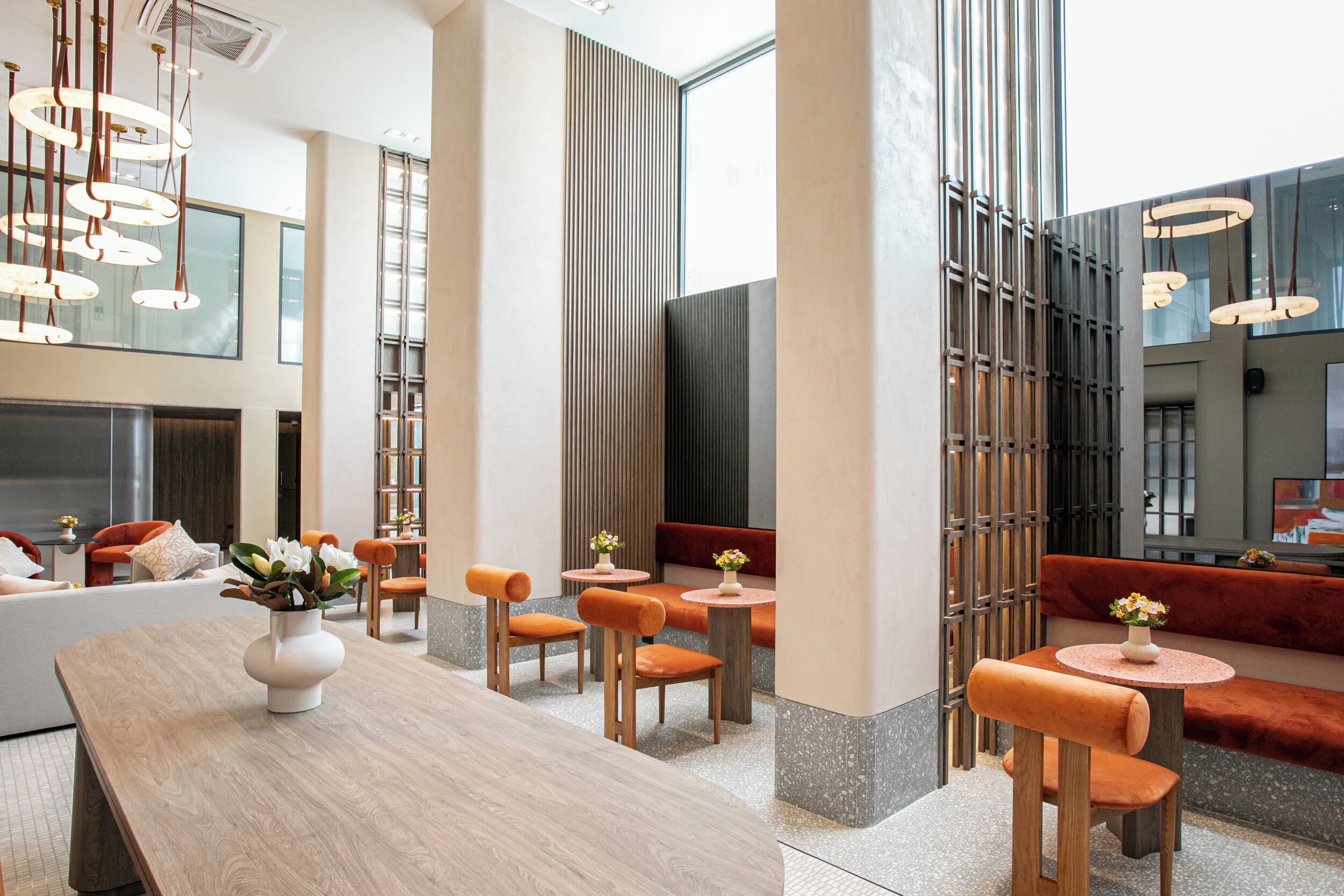 A modern interior with a wooden dining table, orange upholstered chairs, and a seating area with a red sofa.