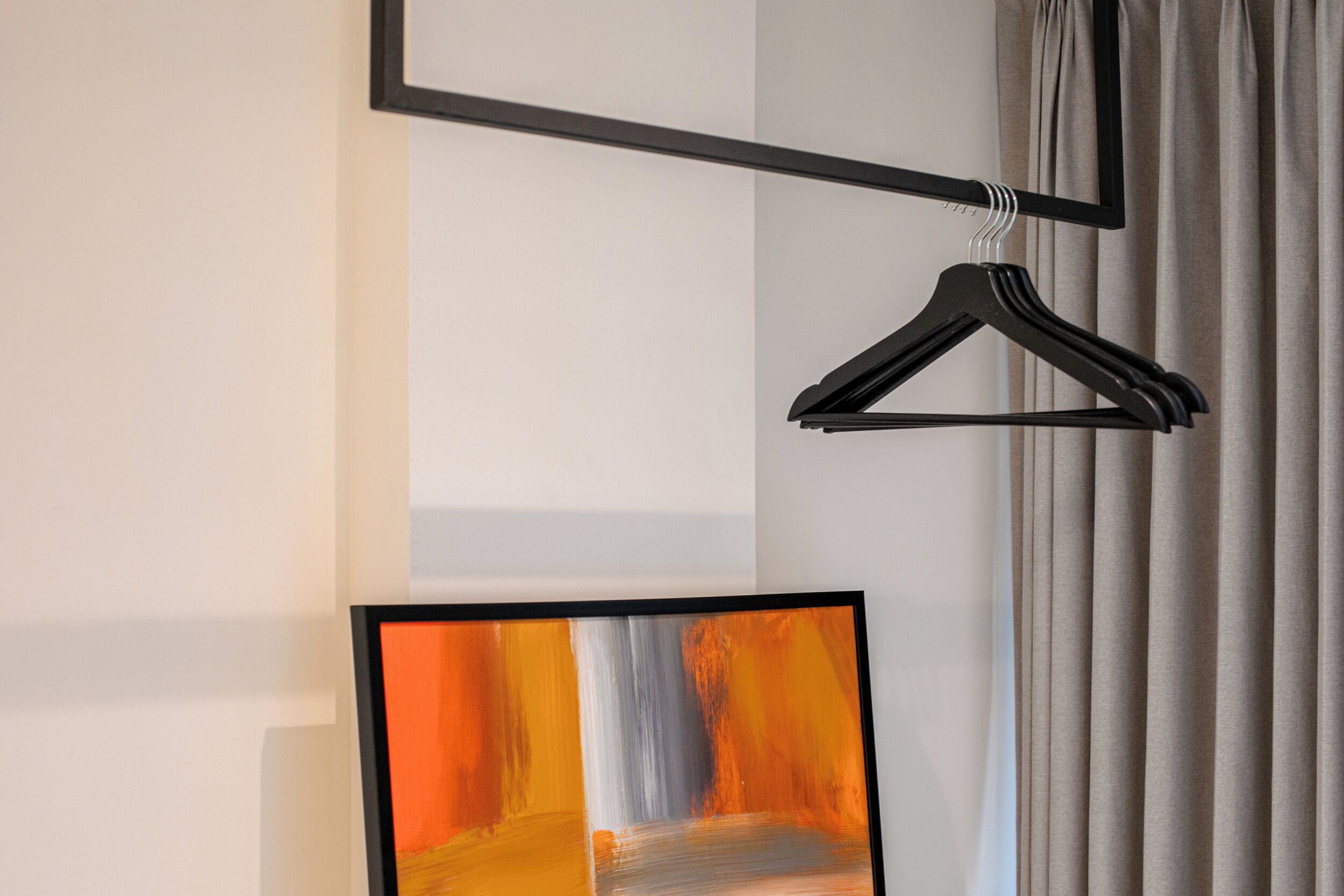 Ein Zimmer mit einem gerahmten abstrakten Gemälde, einem schwarzen Kleiderbügel und einem Vorhang.
