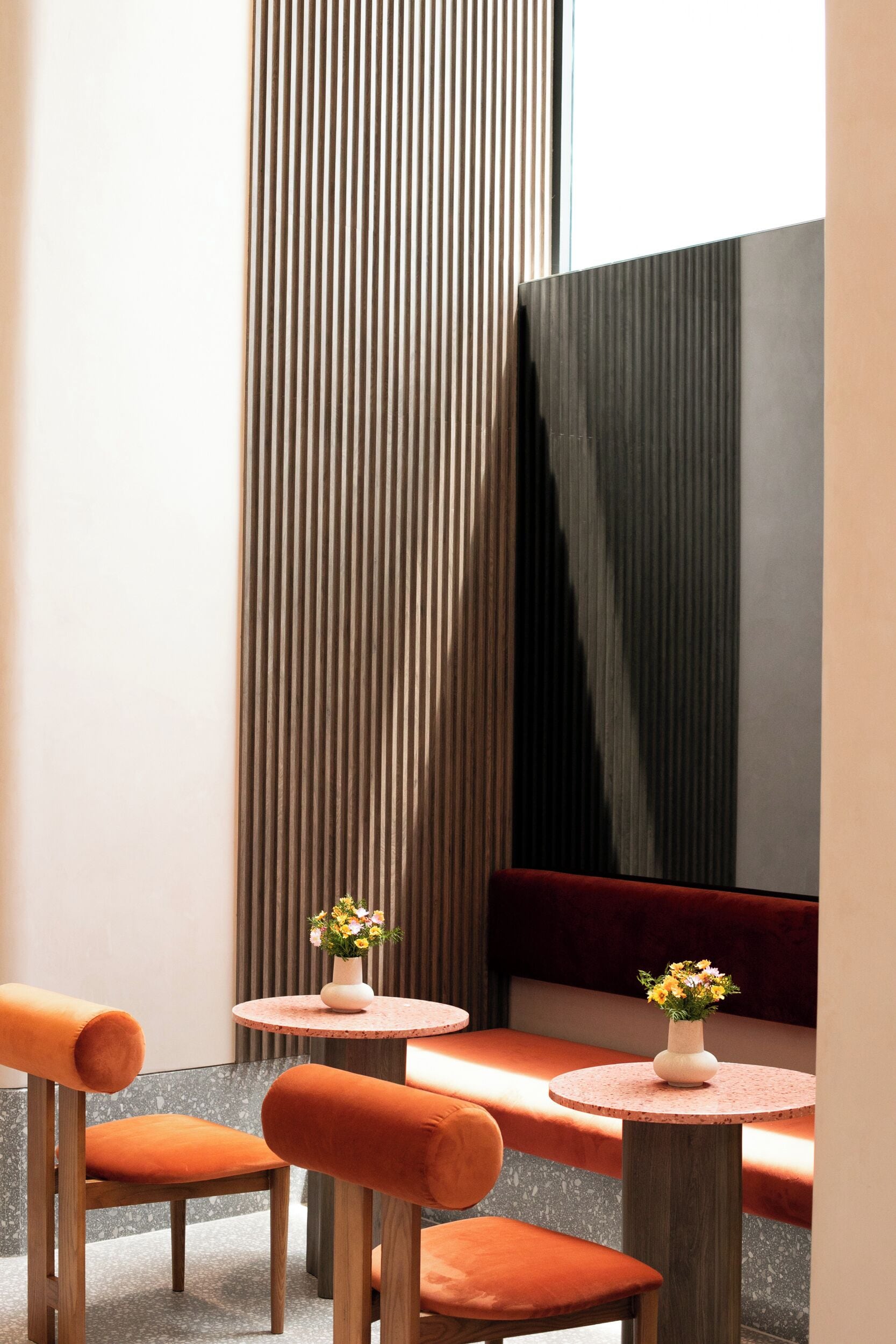 A modern interior with two round tables, orange upholstered chairs, and a vertical wooden slat wall.