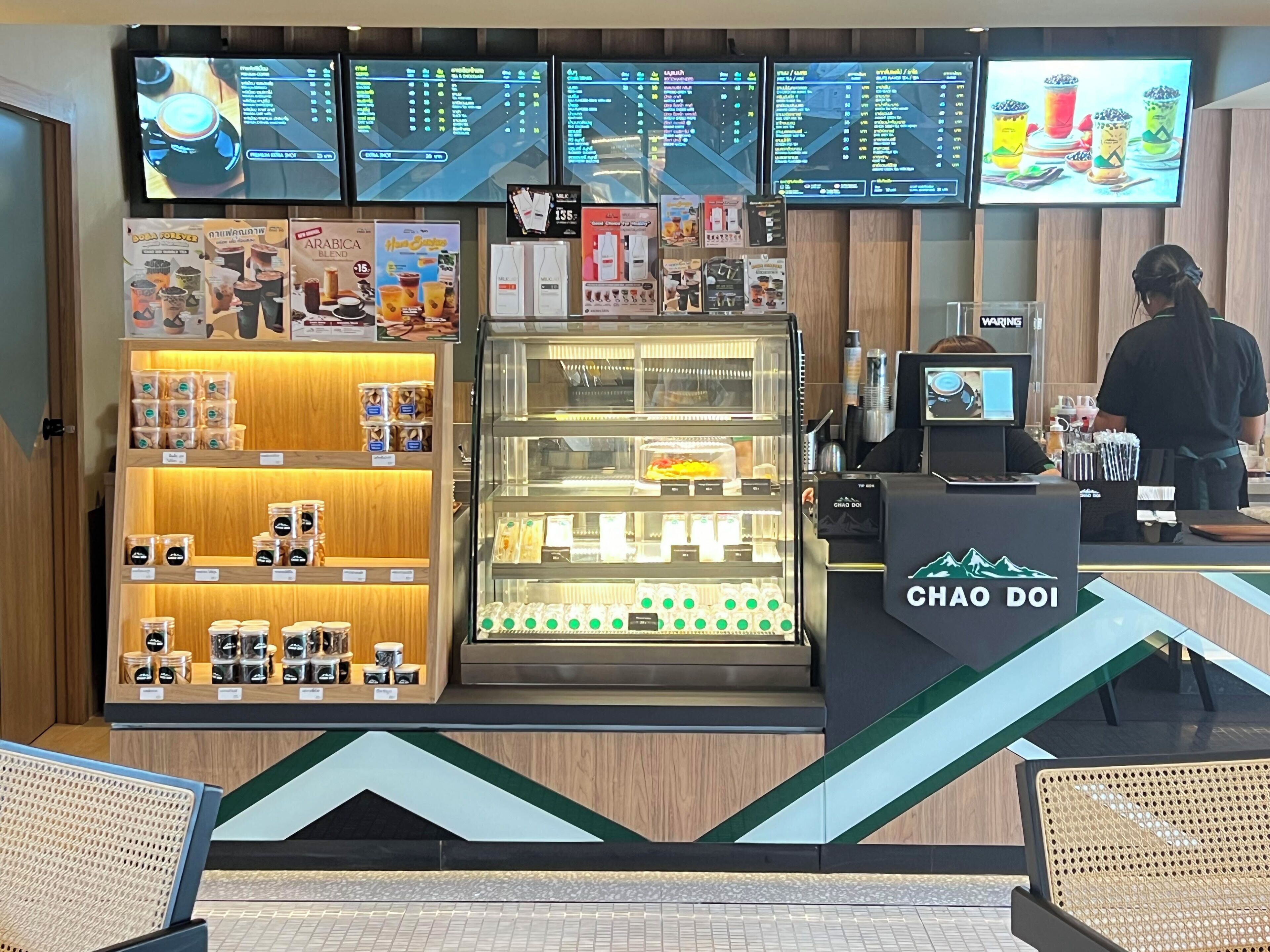Interior de una cafetería con mostrador, carteles de menú y exhibición de productos de café.
