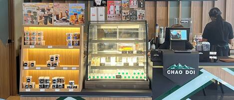 Interior de una cafetería con mostrador, carteles de menú y exhibición de productos de café.