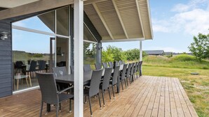 An outdoor patio with a long table and chairs, a covered area with a roof, and a view of the surrounding landscape. - Amazing home in Jerup with sauna (Jerup)