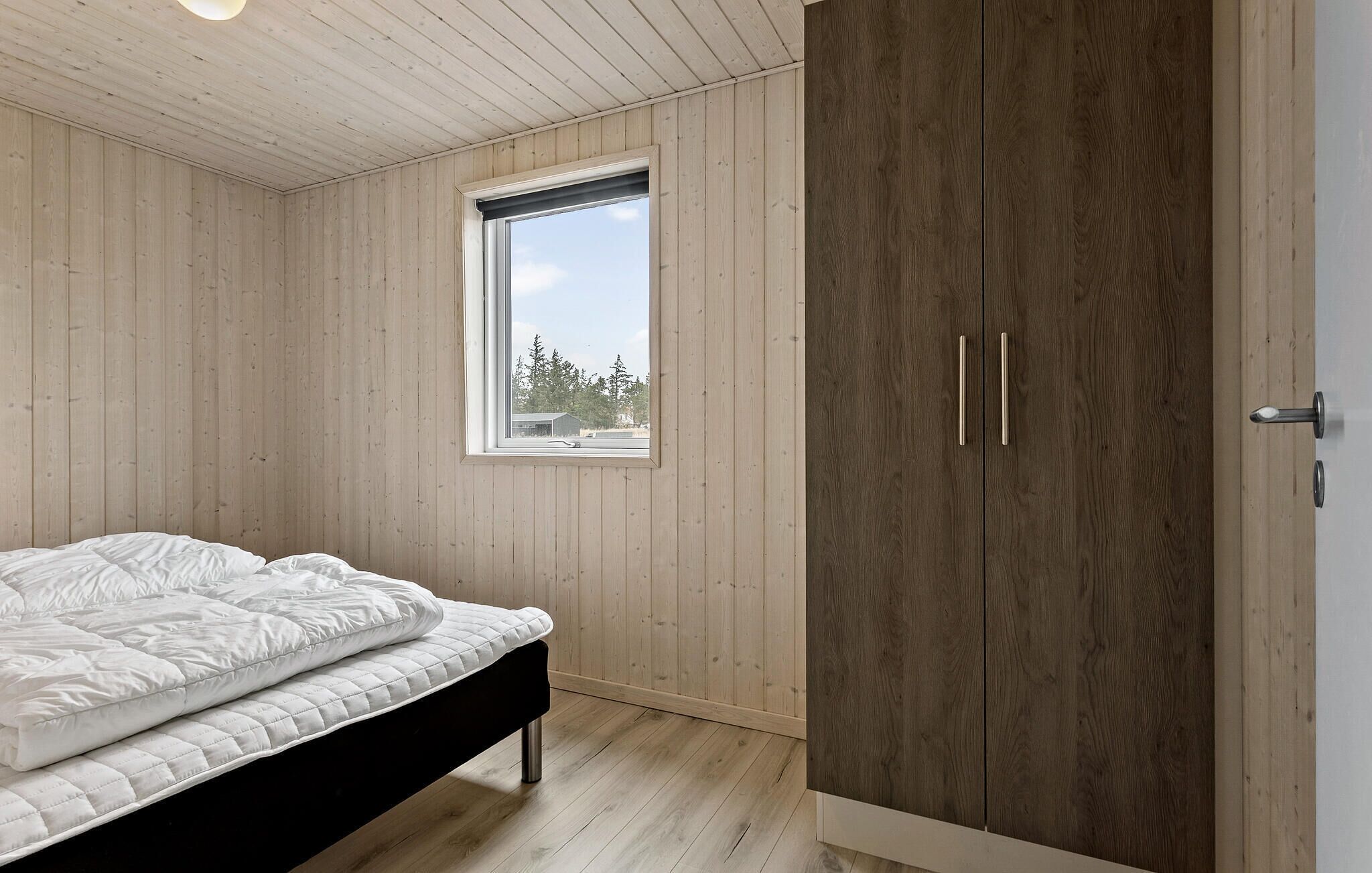 A bedroom with a bed, wooden walls, a window, and a wardrobe.