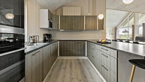 A modern kitchen with wooden cabinets, a stainless steel range, and a large window providing natural light. - Amazing home in Jerup with sauna (Jerup)