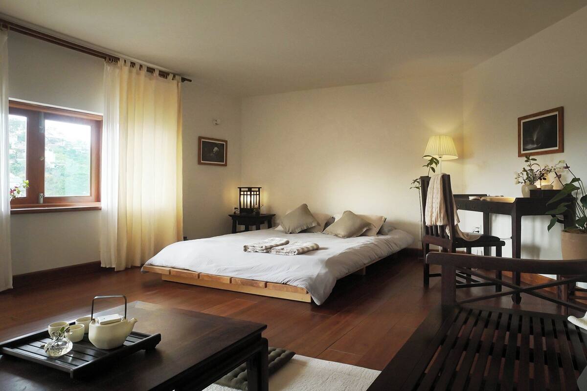 A bedroom with a bed, bedside table, lamp, and a view of the outdoors.