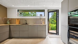 Une cuisine moderne avec des meubles gris, un plan de travail en bois et un four encastré.