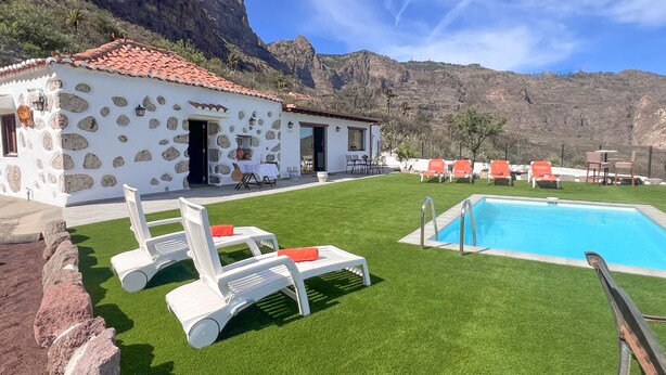 A stone building with a tiled roof, a swimming pool, and outdoor seating.