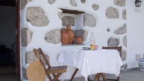 A stone wall with a rustic outdoor seating area, including a table with a white tablecloth, a wicker basket, and a wooden chair.