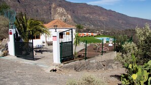 A rustic building with a tiled roof, a fenced patio with lounge chairs, and a pool.