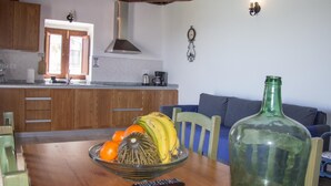 A kitchen with wooden cabinets, a dining table with a bowl of fruit, a remote control, and a green bottle.