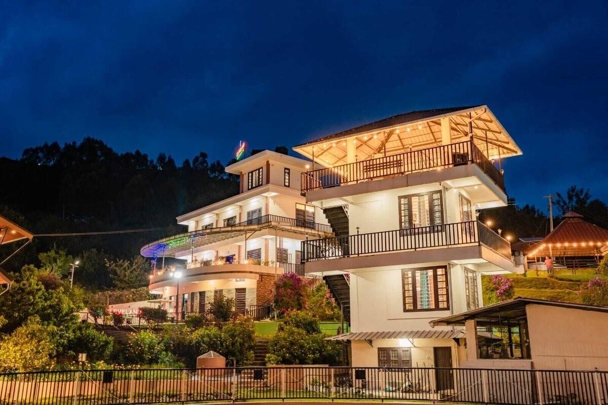 A multi-story hotel with balconies, a well-lit exterior, and a garden area.