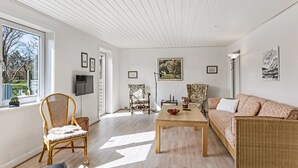 En rummelig stue med stort vindue, træloft og en fletsofa.