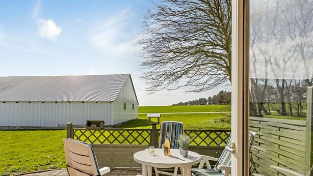 En terrasse med et bord og stole, udsigt til et ladebygning og en græsplæne.