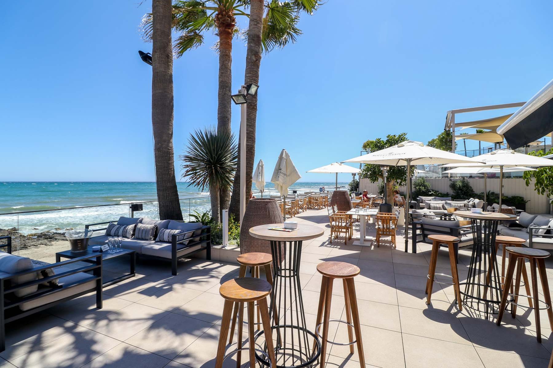 Une terrasse au bord de la plage, avec des sièges extérieurs, des parasols et une vue sur l’océan.