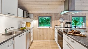 Une cuisine moderne avec un lambris en bois, des appareils électroménagers en acier inoxydable et de grandes fenêtres offrant une vue sur la verdure.