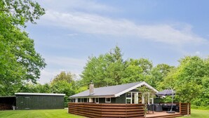 Une cabane en bois dotée d’une terrasse et d’un espace salon extérieur, entourée d’une cour verdoyante et d’arbres.