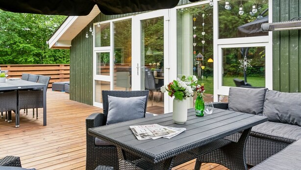 Une terrasse extérieure avec des meubles en osier, une table avec des journaux et un vase rempli de fleurs.