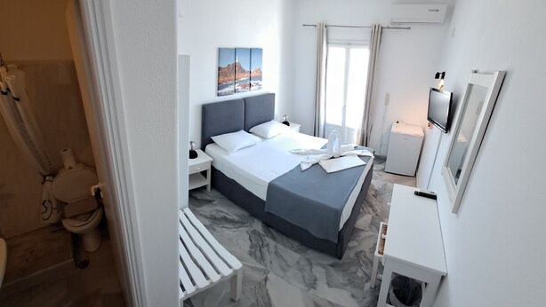 Une chambre d’hôtel moderne, équipée d’un lit, d’un petit bureau, d’une télévision et d’une salle de bain visible à travers une porte ouverte.
