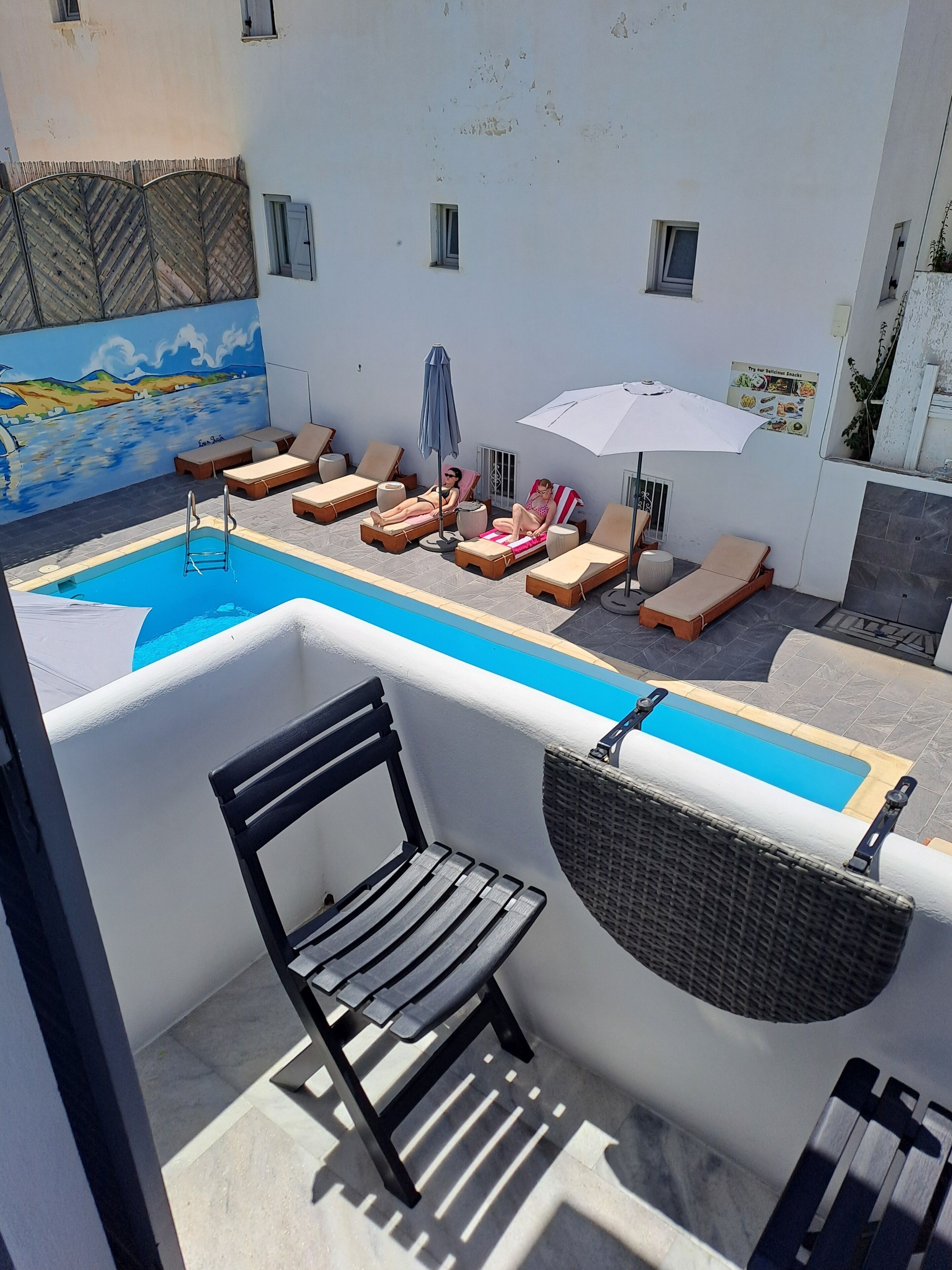 A rooftop pool area with lounge chairs and umbrellas, a small pool, and a mural on the wall.