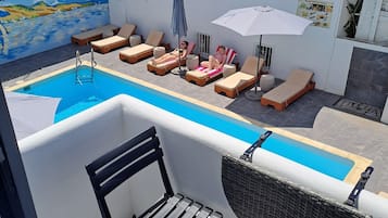 Un área de piscina en la azotea con sillones de descanso y sombrillas, una piscina pequeña y un mural en la pared.